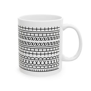 May include: White ceramic mug with a black geometric pattern. The design includes horizontal lines, cross-like shapes, and repeating curved and angular elements. The mug has a curved handle.