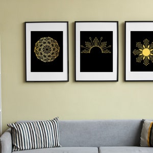 Op de afbeelding: Drie ingelijste zwart-wit prints met gouden geometrische ontwerpen. De ontwerpen zijn een mandala, een zon en een bloem.
