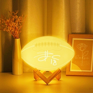May include: A white football-shaped night light with a wooden stand. The football has a stitched design and the number "18" written on it.