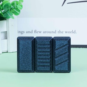 Op de afbeelding: Drie donkerblauwe rechthoekige tegels met verschillende textuurpatronen. De tegels zijn gemaakt van een getextureerd materiaal dat lijkt op een fijne glitter.