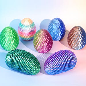 Puede incluir: Siete huevos de drag&oacute;n decorativos en varios colores, incluyendo verde, azul y tonos arco&iacute;ris. Los huevos tienen superficies texturizadas en forma de escamas y est&aacute;n dispuestos sobre un fondo claro. Un art&iacute;culo decorativo de tem&aacute;tica fant&aacute;stica.