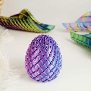 May include: A decorative, iridescent egg-shaped sculpture in shades of purple and blue. The egg is constructed from interwoven, diamond-shaped segments. Other similar, colorful, wing-like shapes are in the background.