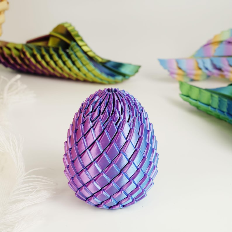 May include: A decorative, iridescent egg-shaped sculpture in shades of purple and blue. The egg is constructed from interwoven, diamond-shaped segments. Other similar, colorful, wing-like shapes are in the background.