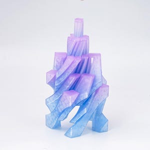Peut inclure: Une sculpture imprimée en 3D aux tons bleus et violets, ressemblant à une forme architecturale stylisée. L'objet présente un design en couches avec des formes géométriques et un dégradé de couleurs, créant une esthétique moderne.