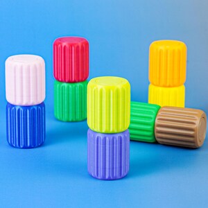 Può includere: Una collezione di contenitori cilindrici in plastica con coste verticali in vari colori solidi, tra cui rosa, blu, rosso, verde, giallo, verde lime, viola e marrone, disposti in coppie impilate e unità singole su una superficie blu.