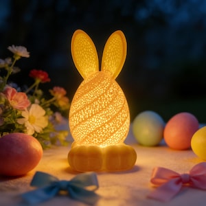 May include: A glowing Easter bunny-shaped lamp with a textured, egg-shaped body and long ears. The lamp emits a warm, yellow light, and is surrounded by pastel-colored Easter eggs and bows. The lamp is a decorative item for the Easter holiday.