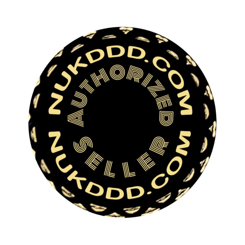 May include: A black circular sticker with gold text. The text reads "NUKDDD.COM AUTHORIZED SELLER NUKDDD.COM" in a circular pattern. The sticker has a textured border and a solid black center.