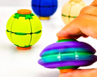 May include: A collection of spherical fidget toys featuring segmented panels. One toy is lime green with orange caps, another is blue with yellow caps, one is cream-colored, and a purple and teal gradient toy is held in the foreground.