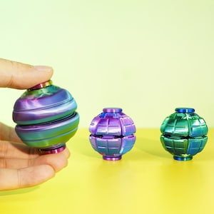 May include: Three spherical fidget toys with a metallic iridescent finish. The left sphere has smooth horizontal grooves, while the two smaller spheres on the right feature a grid-like pattern. All items display a gradient of purple, blue, and green.