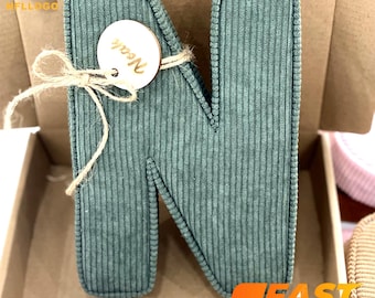 May include: A green corduroy letter N with a wooden tag that says "Noah" tied to it with twine.