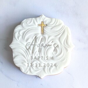 May include: White fondant cookie with a swirl design, a gold cross, and the text "Adam's Baptism 13.11.2024".