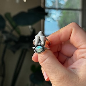 May include: A silver ring with a white tooth charm and a green abalone shell stone.