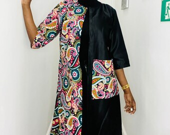 May include: A long-sleeved dress with a black collar and a black pocket on the right side. The dress features a paisley pattern in black, pink, green, and yellow.