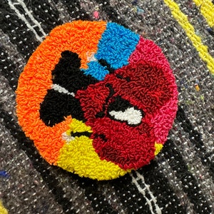 May include: A colorful, round rug with a black, white, and red design. The rug is made of yarn and has a fuzzy texture.