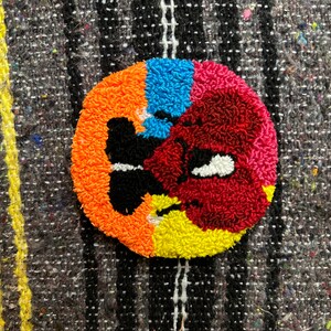 May include: A colorful round rug with a butterfly design in the center. The rug is made of yarn and has a textured surface. The colors are orange, yellow, red, blue, and black.