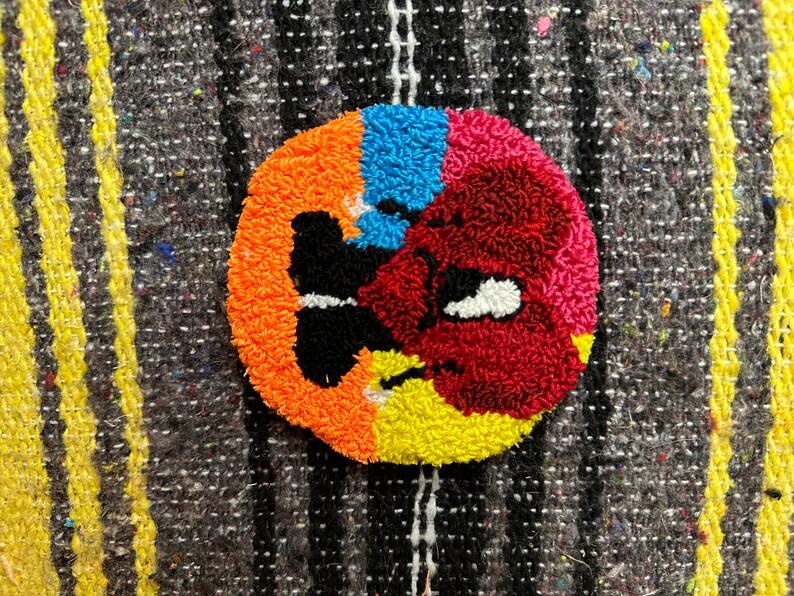 May include: A colorful round rug with a butterfly design in the center. The rug is made of yarn and has a textured surface. The colors are orange, yellow, red, blue, and black.