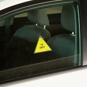 May include: A yellow triangle-shaped car window sign with the text "I'M EMPTY" inside. The sign is attached to the window of a car.