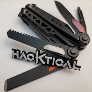 Könnte beinhalten: Schwarzes Multitool mit Säge, Messer und Feile. Der Text "HACKTICAL" ist weiß. Die Messerklinge hat rote und blaue Akzente. Das Werkzeug ist für vielfältige Zwecke konzipiert.