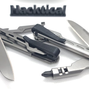 Puede incluir: Una herramienta multiusos plateada con un mango negro y una hoja que dice "GERBER". La herramienta est&aacute; abierta y la hoja est&aacute; extendida. La herramienta est&aacute; sobre una superficie blanca.