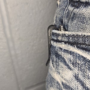 Puede incluir: Un cuchillo de bolsillo negro con un clip est&aacute; metido en el bolsillo delantero de un par de pantalones vaqueros de mezclilla azul claro.