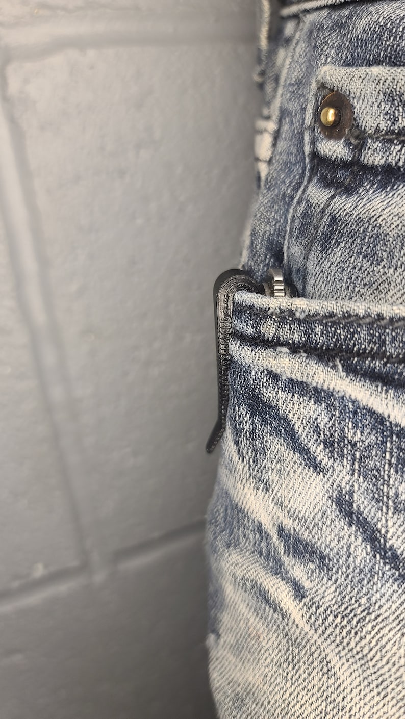 Puede incluir: Un cuchillo de bolsillo negro con un clip est&aacute; metido en el bolsillo delantero de un par de pantalones vaqueros de mezclilla azul claro.