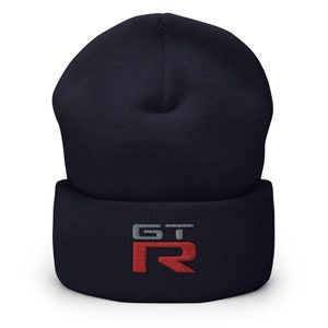 Puede incluir: Un gorro de punto azul marino con un logotipo "GT-R" bordado en rojo y gris.