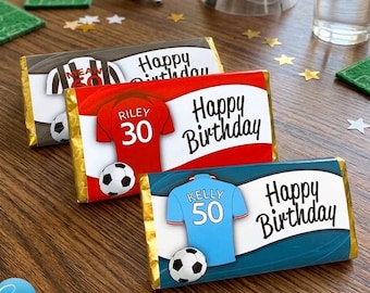 May include: Three rectangular chocolate bars wrapped in custom paper featuring soccer themes. Each wrapper displays a jersey graphic with a name and number, a soccer ball, and the text Happy Birthday in black script against red, blue, or grey.
