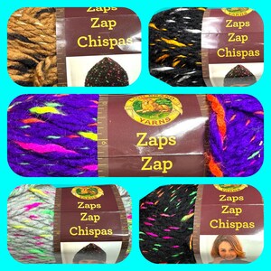 May include: Four skeins of Lion Brand Zaps Zap yarn in different colour combinations. The yarn is a multi-coloured, speckled yarn with a fuzzy texture. The yarn labels feature the Lion Brand logo and the text "Zaps Zap" and "Chispas".