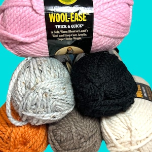 May include: A stack of various colored yarn skeins, including pink, gray, orange, black, brown, and cream. The pink skein has a label that reads "WOOL-EASE THICK & QUICK". The yarn is a soft, warm blend of lamb's wool and acrylic.