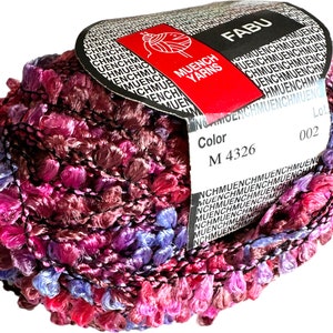 May include: A skein of pink, purple, and blue yarn with a black label that reads "FABU" and "MUENCH YARNS". The label also includes the color code "M 4326" and the lot number "002".
