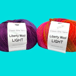 May include: Two skeins of Liberty Wool Light yarn in shades of purple and red-orange. Each skein has a white label with the brand name and product details. The yarn is 100% washable wool, perfect for knitting and crochet projects.