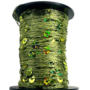 May include: A spool of green thread with iridescent sequins. The thread is wound around a black plastic spool.