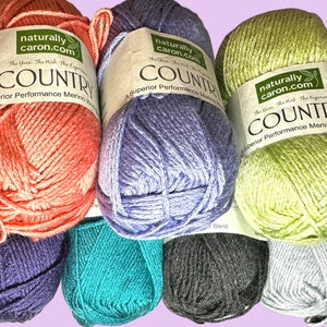 May include: Six skeins of yarn in various colors, including coral, lavender, teal, gray, and light green. Each skein has a label that reads "naturally caron.com" and "COUNTRY Superior Performance Merino Wool".