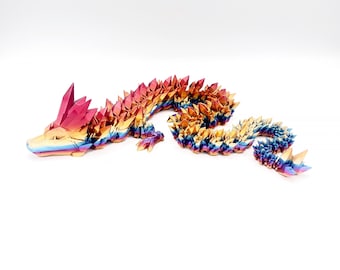 May include: A colorful origami dragon made of iridescent paper. The dragon is curled up in a resting position with its head raised. The dragon's scales are a mix of red, orange, yellow, green, blue, and purple.