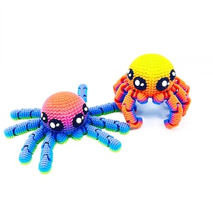 Op de afbeelding: Twee kleurrijke gehaakte octopus speelgoedjes. E&eacute;n is regenboogkleurig met blauwe tentakels en de andere is geel, oranje en rood met oranje tentakels.