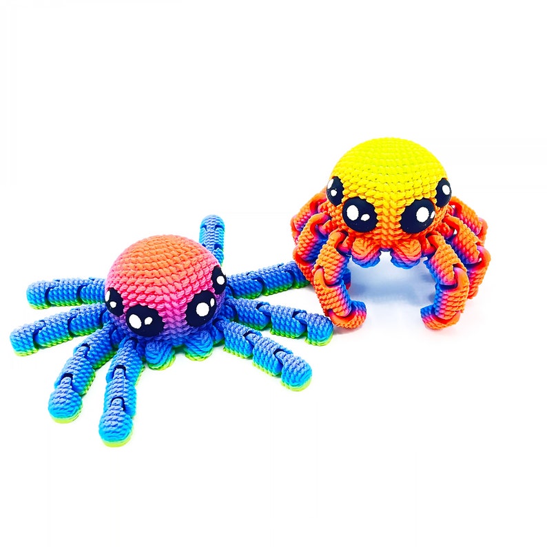 Op de afbeelding: Twee kleurrijke gehaakte octopus speelgoedjes. E&eacute;n is regenboogkleurig met blauwe tentakels en de andere is geel, oranje en rood met oranje tentakels.
