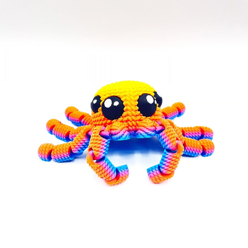 Op de afbeelding: Een klein, kleurrijk octopus speelgoed gemaakt van gehaakt garen. De octopus is geel met oranje en blauwe tentakels en heeft grote zwarte ogen.