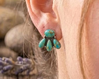 May include: A silver-toned stud earring featuring a cluster of turquoise stones. The earring has an oval top stone and three teardrop-shaped stones below, all set in a decorative silver frame. The turquoise stones have natural variations in color.
