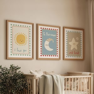 May include: Three framed art prints with a nursery theme. The prints feature a smiling sun with "i love you", a crescent moon with "To the moon", and a star with "and back". Each print has a decorative border and is in a gold frame.