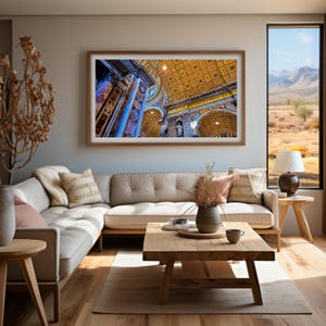 Op de afbeelding: Een witte hoekbank met een houten salontafel ervoor. Een ingelijst schilderij van een kathedraalplafond met gouden en blauwe accenten hangt aan de muur achter de bank. Een raam met uitzicht op een bergketen en een woestijnlandschap bevindt zich rechts van de bank.