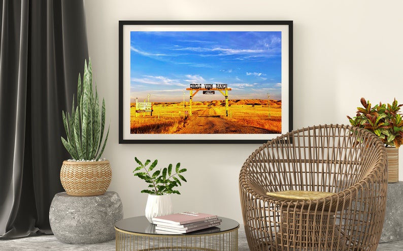 May include: A framed photograph of a rustic wooden gate with the words "Circle View Ranch" painted on it. The gate is open and leads to a dirt road that goes through a field of golden grass. The sky is blue with white clouds.