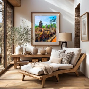 May include: A wooden chaise lounge with white cushions and a throw blanket in a living room setting. A framed print of a stone sculpture with a blue sky background hangs on the wall above a wooden shelf with decorative vases.