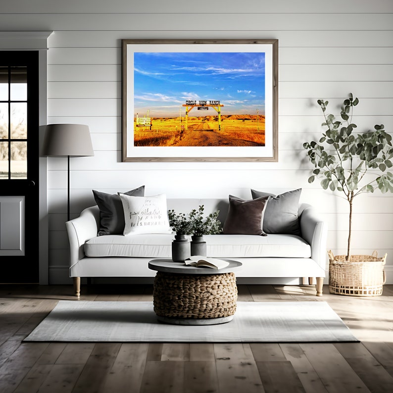 May include: A framed photograph of a rustic wooden gate with the words "Circle View Ranch" on a sign. The gate is open and leads to a dirt track that goes through a field of tall grass. The sky is blue with white clouds.