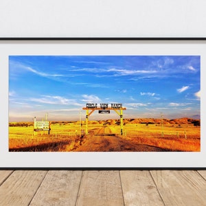 May include: A panoramic view of a rural landscape with a wooden sign that reads "Circle View Ranch" above a dirt road leading into a field of golden grass. The sky is blue with white clouds.