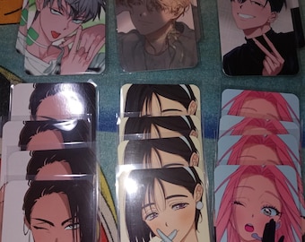 May include: A collection of anime-style character art cards. The cards feature various characters with different hairstyles and expressions. The color palette includes shades of gray, black, pink, and green. Each card is encased in a clear protective sleeve.