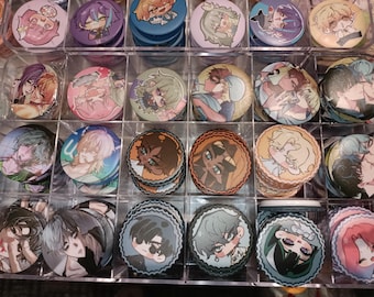 Puede incluir: Una colección de pines redondos de colores con varios personajes de dibujos animados y diseños. Los pines están dispuestos en un patrón de cuadrícula sobre una superficie blanca.