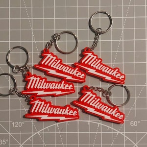 Könnte beinhalten: Fünf rote und weiße Milwaukee-Schlüsselanhänger mit silbernen Schlüsselringen. Jeder Schlüsselanhänger zeigt das Milwaukee-Logo mit einem Blitzdesign. Die Schlüsselanhänger sind auf einer grauen Rasteroberfläche angeordnet.