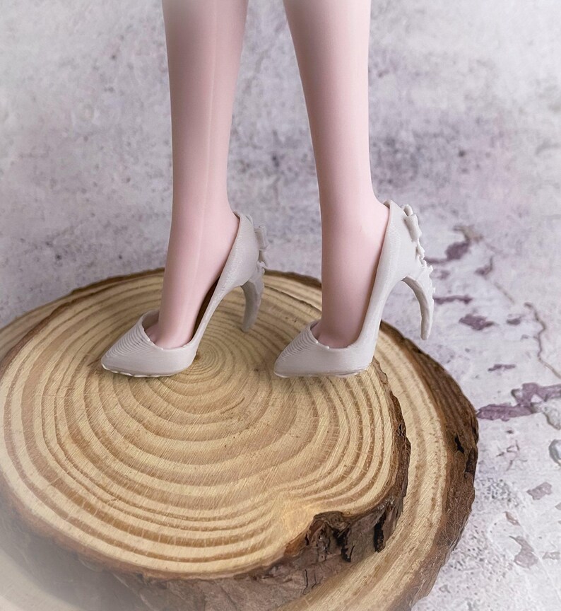 May include: A pair of light gray high-heeled shoes with a unique design. The heels have a curved shape with decorative elements. The shoes are on a wooden surface, showcasing the footwear's details and style.