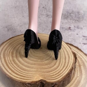 以下が含まれることがあります： ユニークなデザインの黒いハイヒール。ヒールは円錐形で、靴のアッパーには装飾的な要素があります。靴は木製の表面に展示されています。