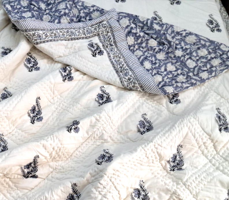 Puede incluir: Una colcha de algod&oacute;n blanco con un estampado floral azul. La colcha est&aacute; doblada por la mitad y tiene una textura acolchada.